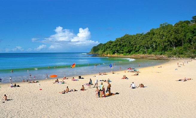 A sandy beach bustling with lots of people enjoying the sunshine coast sightseeing.