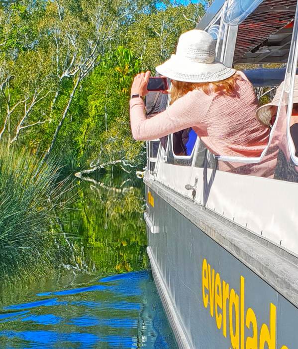A woman is taking a picture from the side of a boat during a Sunshine Coast sightseeing tour.