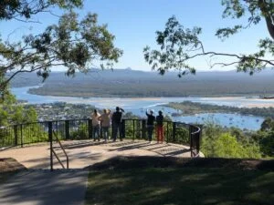 A group of people on a sunshine coast day trip, standing on a hill overlooking a river.