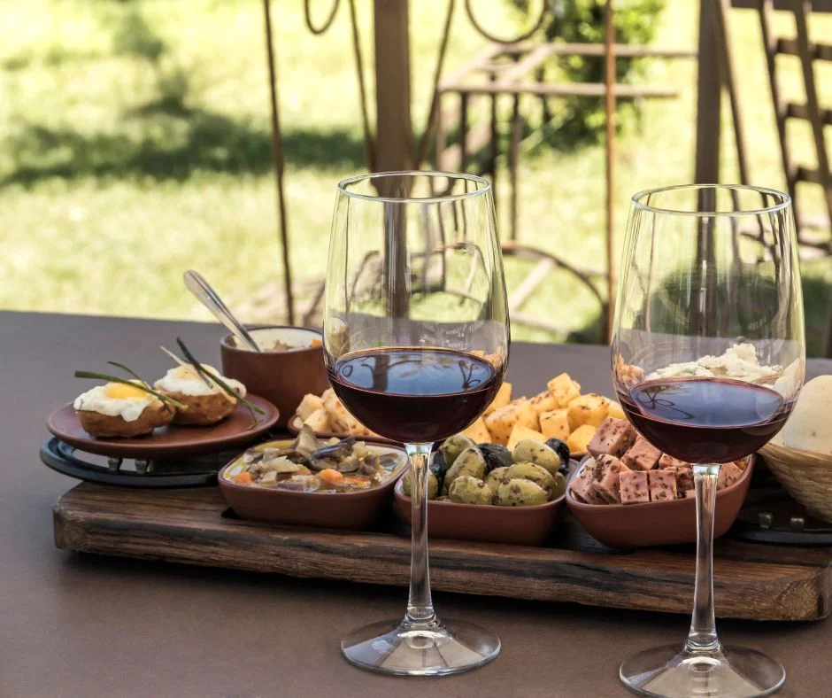 A delightful spread of food and two glasses of wine are beautifully presented on a rustic wooden tray on a Hinterland tour.