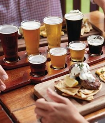 A group of people enjoying beer on a wooden tray during a Sunshine Coast wine tour.