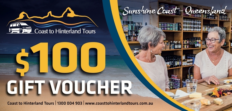 An advertisement for Coast to Hinterland Tours featuring a $100 gift voucher. The image shows two women smiling at a dining table with shelves of condiments in the background. The text includes a phone number, website, and mentions "Sunshine Coast - Queensland." Gift Vouchers available now!